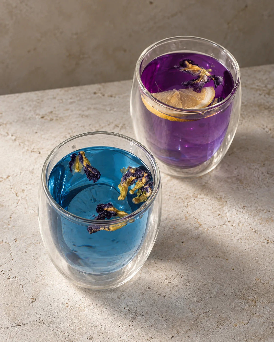 Two glasses of butterfly pea flower tea showing its color change: blue tea and purple tea with lemon.