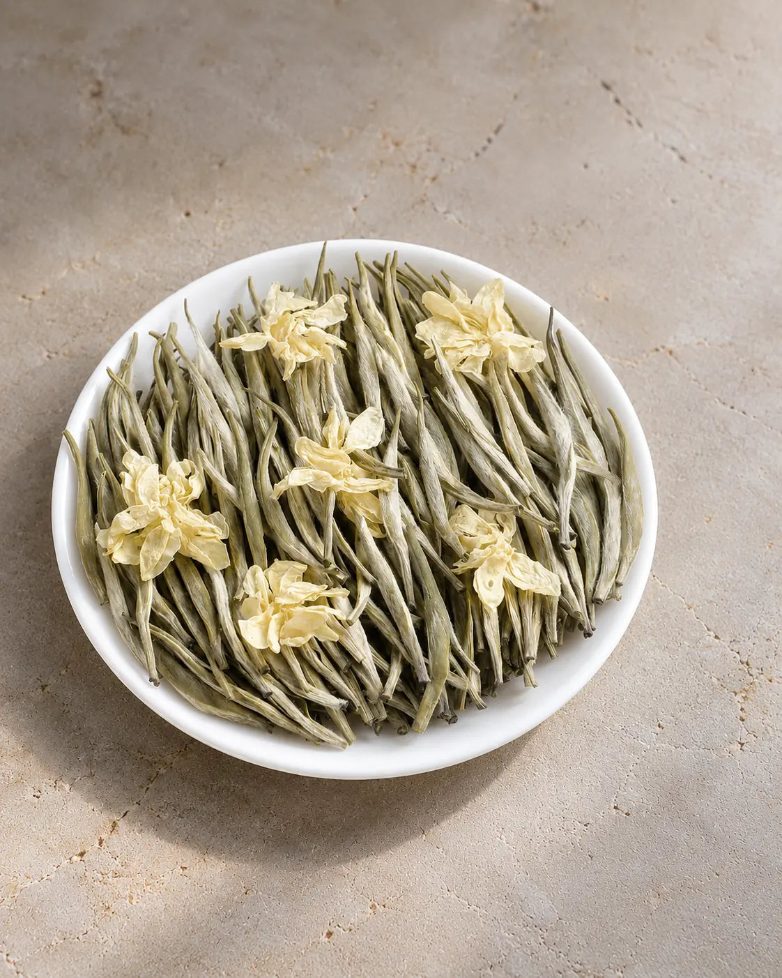 Jasmine Snow loose-leaf green tea from Mengding Mountain, with silvery buds and dried jasmine blossoms on a white plate.
