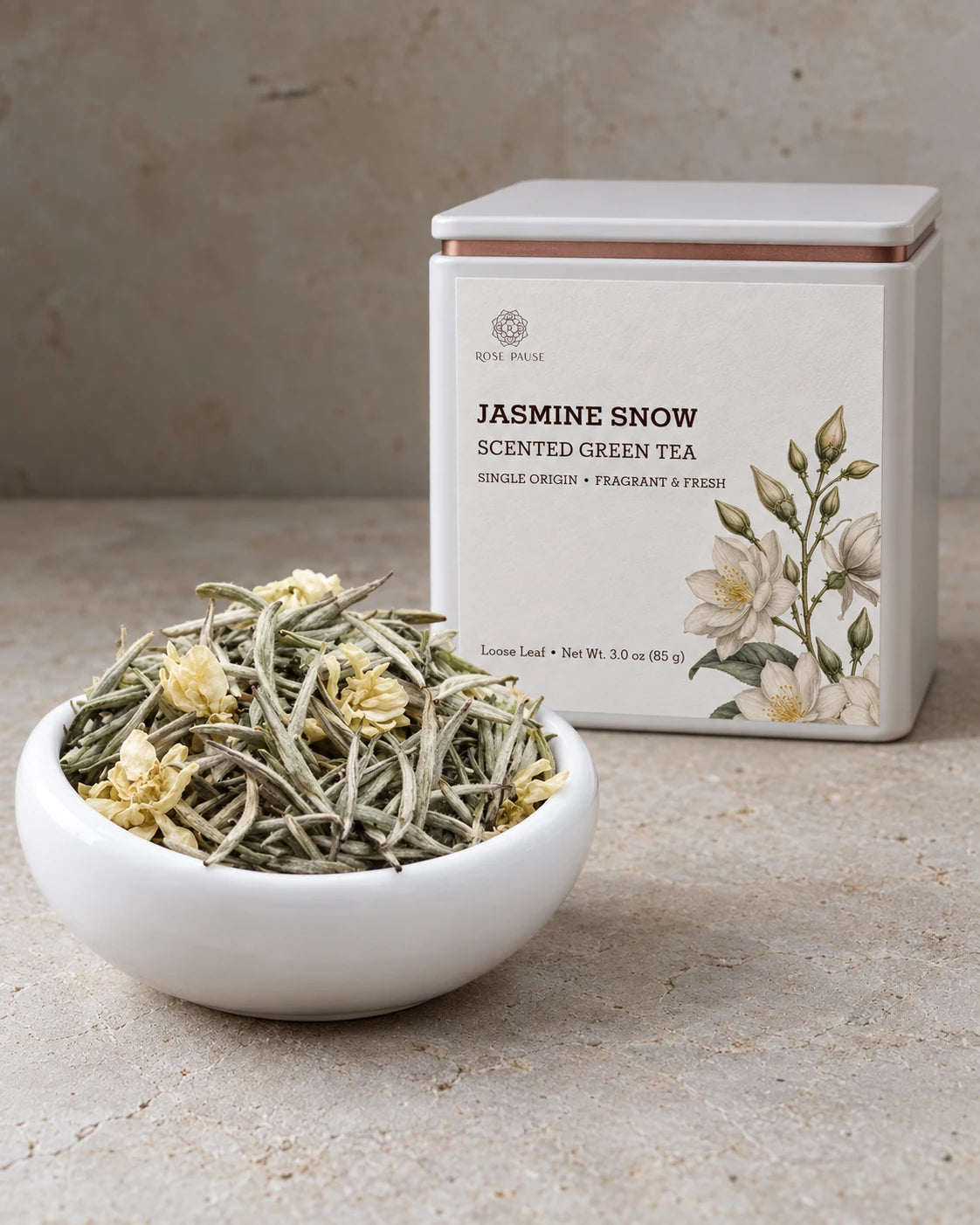 Rose Pause Jasmine Snow loose-leaf jasmine green tea in an illustrated tin beside a white bowl of tea buds and blossoms.