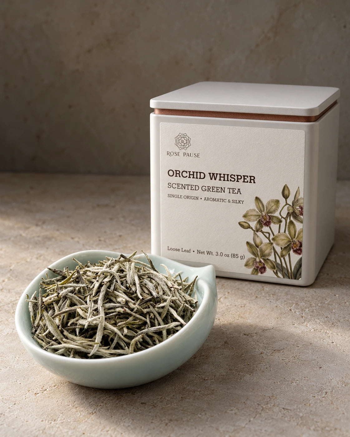 Rose Pause Orchid Whisper loose-leaf orchid green tea in an illustrated tin beside a pale green dish of silvery tea buds.