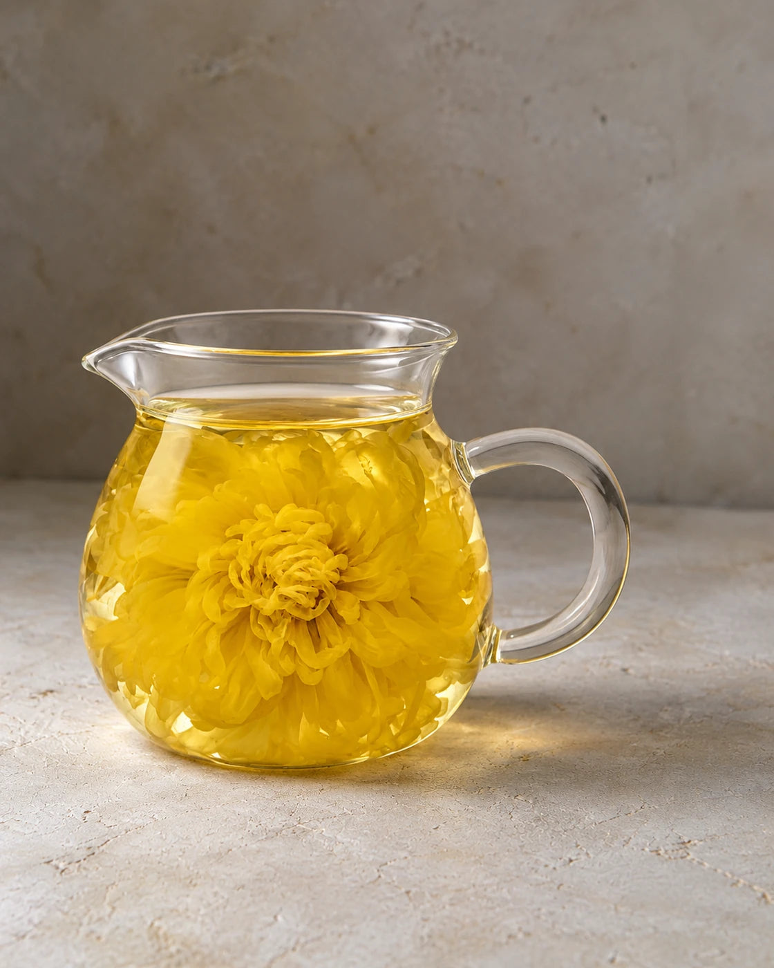 Royal chrysanthemum tea in a clear glass pitcher, with a whole yellow flower unfurled in the golden infusion.