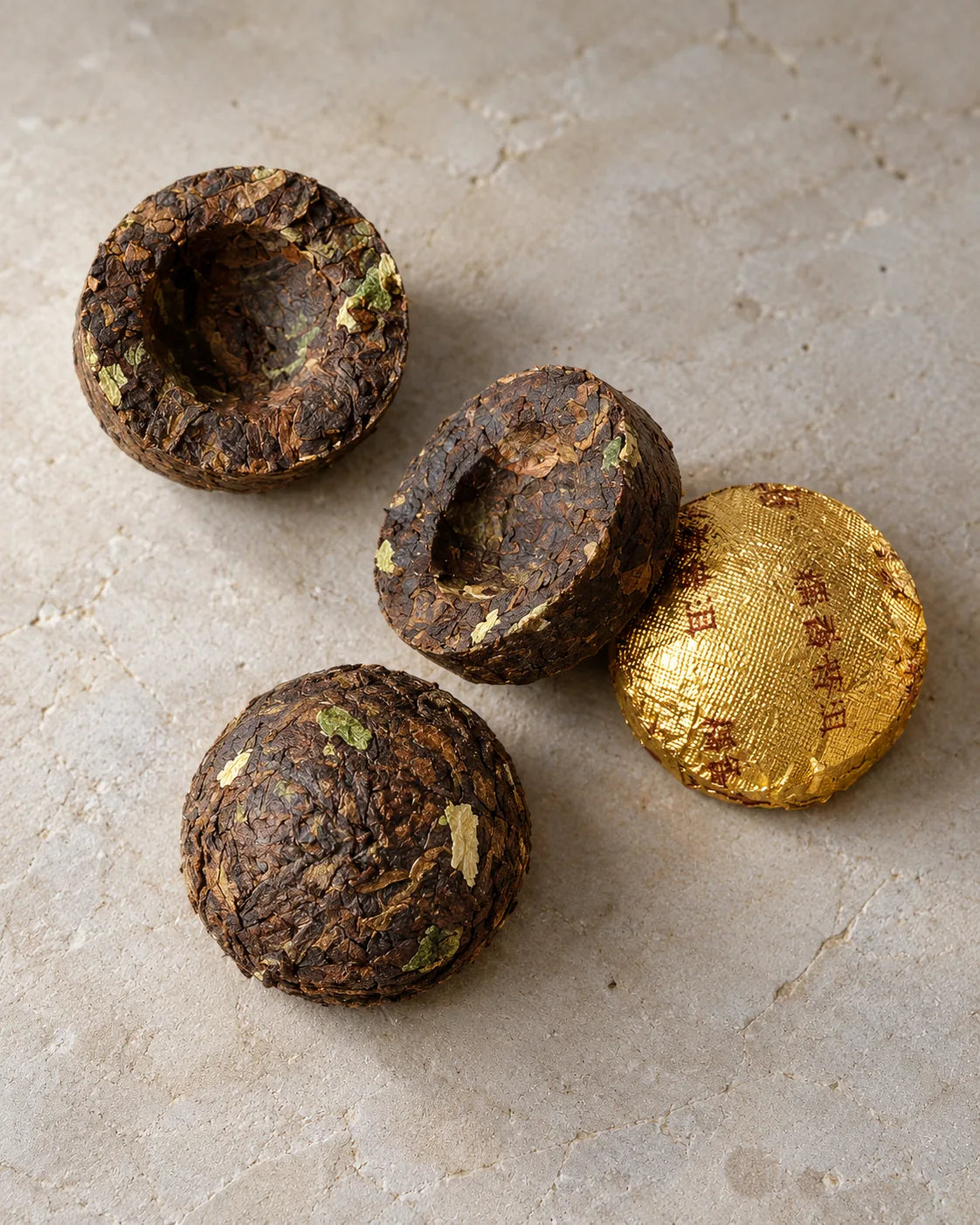 Three bare sticky rice pu-erh mini tuo cha show rounded tops and recessed centers beside a gold-wrapped piece.