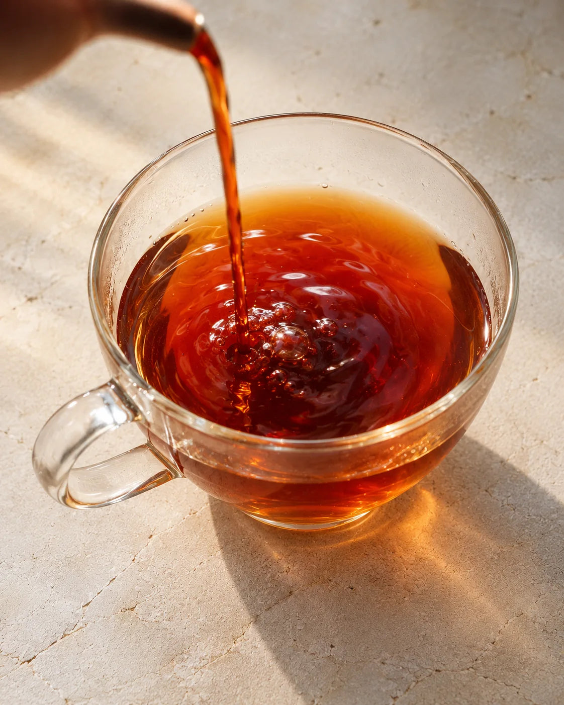 A stream of ruby-red sticky rice pu-erh tea pouring into a glass cup, creating bubbles and ripples.
