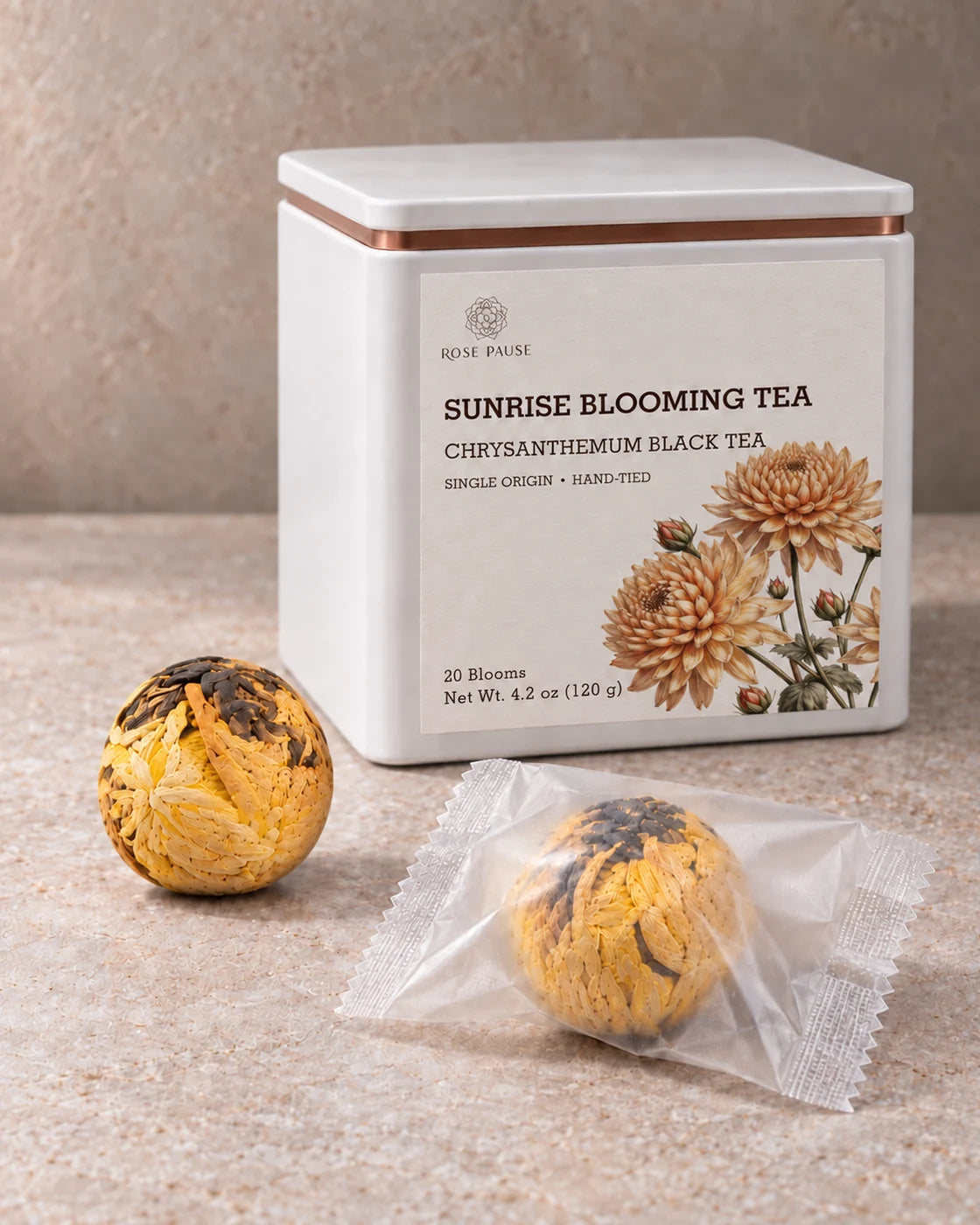 Rose Pause Sunrise Blooming Tea tin beside two chrysanthemum black tea balls, one individually wrapped.