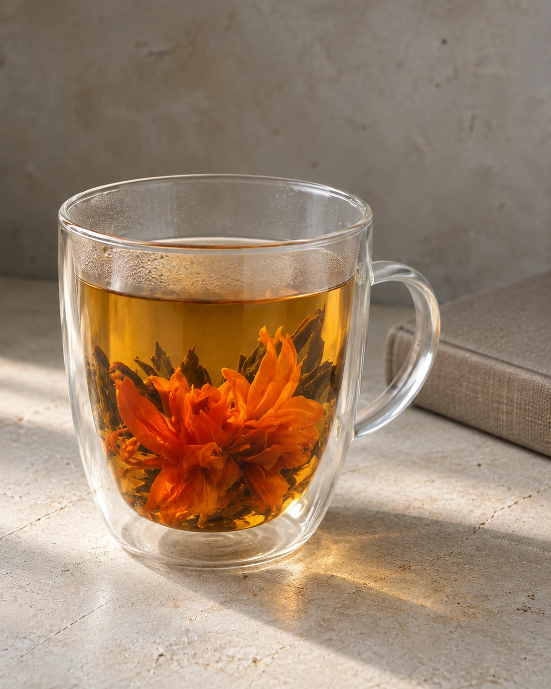 Orange lilies opening among black tea leaves in a double-walled glass mug filled with amber tea.