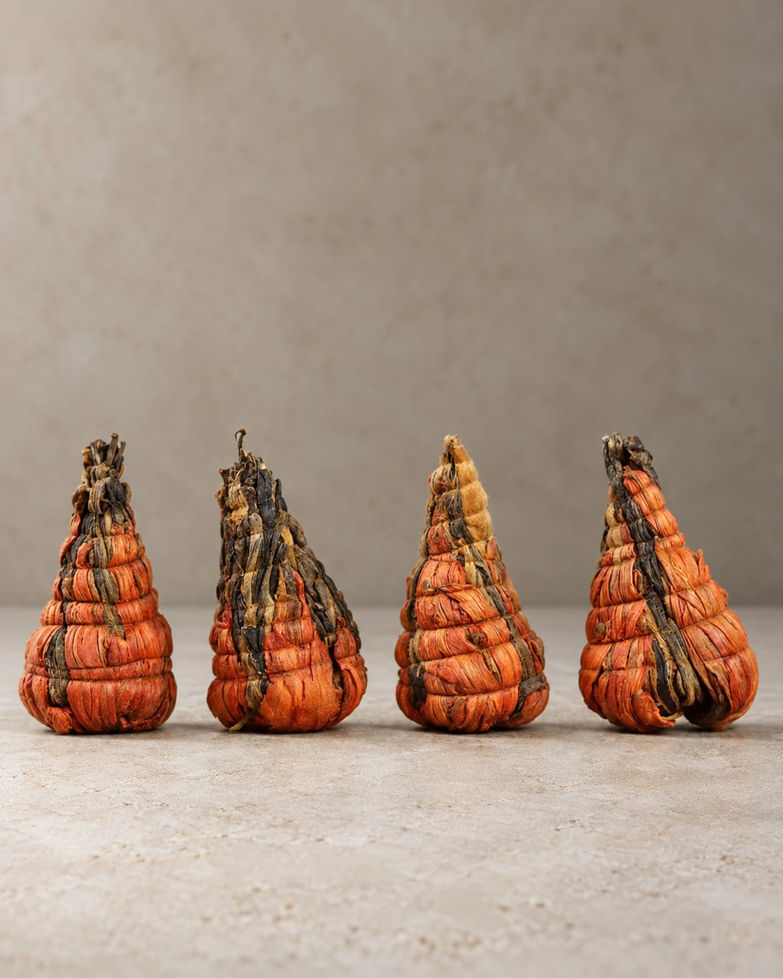 Four cone-shaped, hand-tied tea bundles made with orange lily petals and Yunnan black tea, standing in a row.