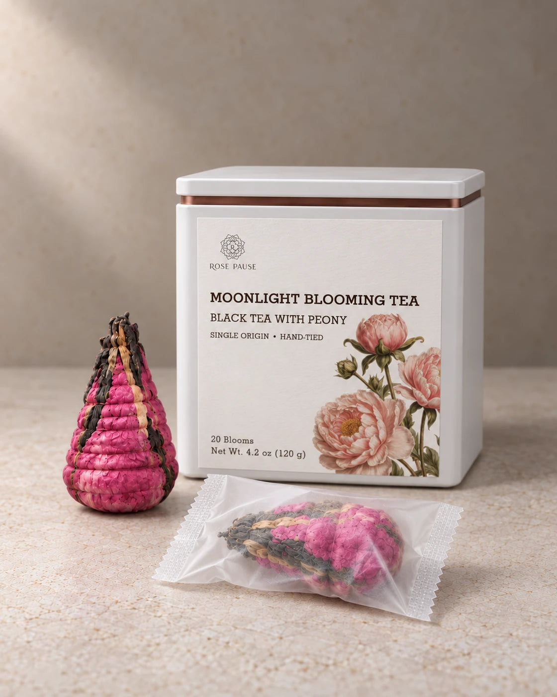 Rose Pause Moonlight Blooming Tea tin beside two hand-tied pink peony tea blooms, one individually wrapped.