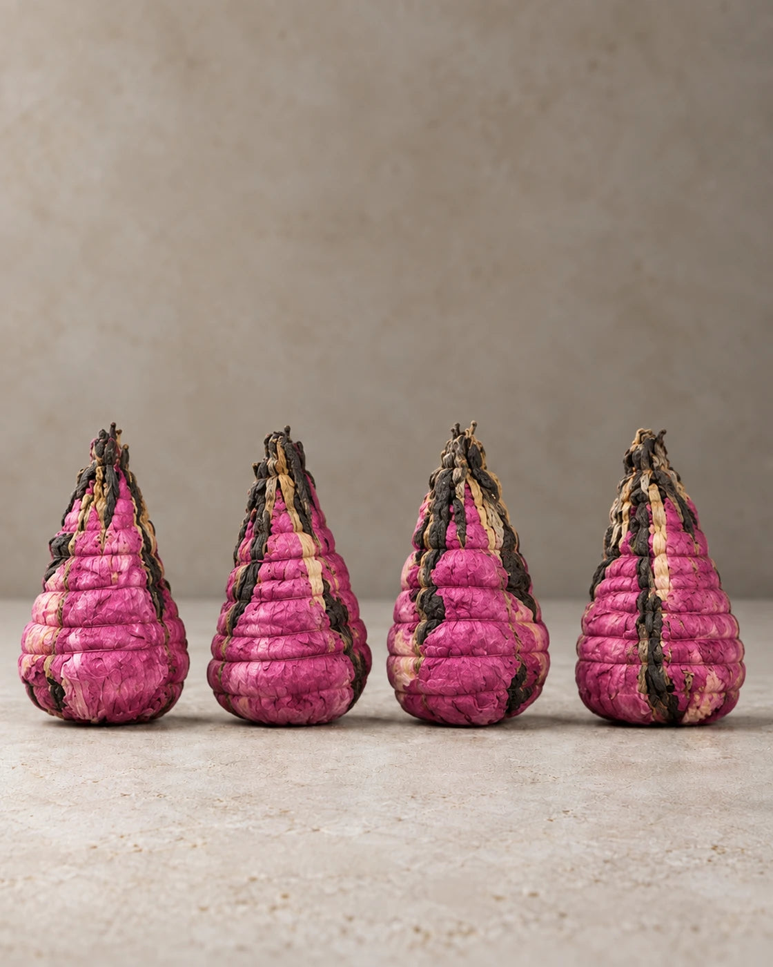 Four cone-shaped, hand-tied tea bundles made with pink peony petals and Yunnan black tea, standing in a row.