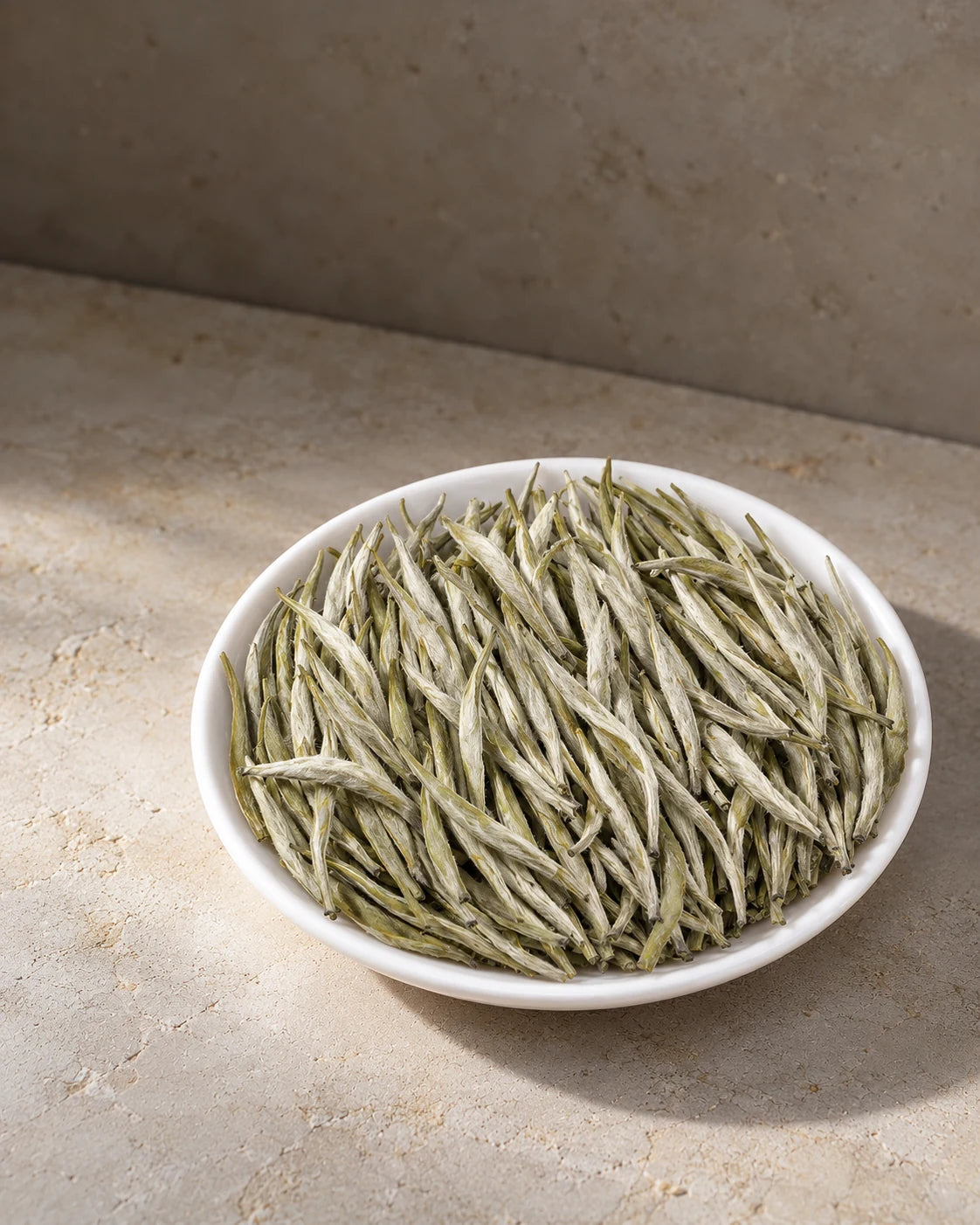 Orchid Whisper loose-leaf green tea from Mengding Mountain, with slender, silvery buds piled on a white plate.