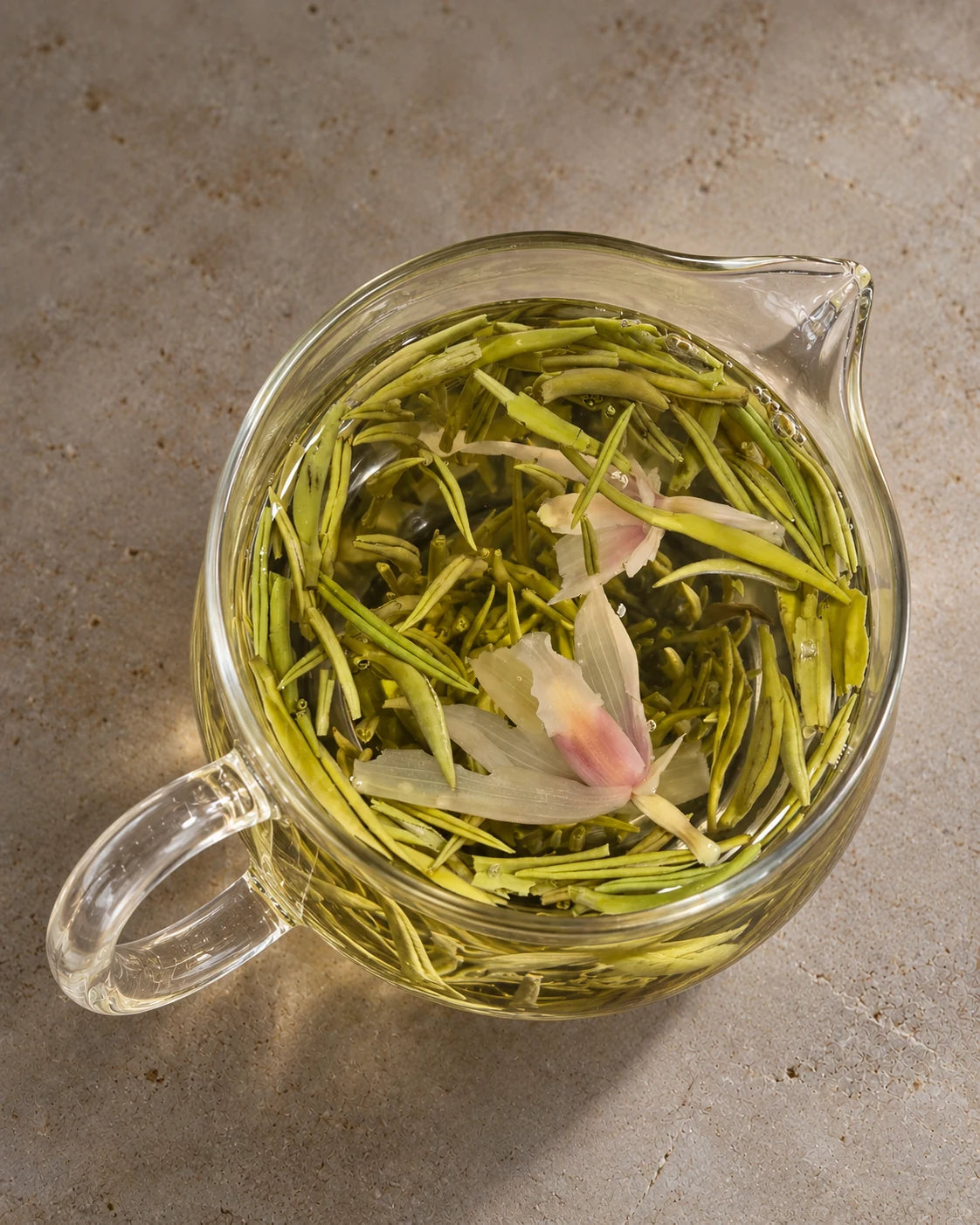 Overhead view of orchid green tea steeping in a clear glass pitcher, with slender tea buds and orchid blossoms in golden tea.