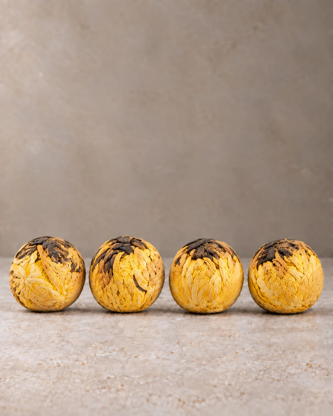 Four hand-tied blooming tea balls made with golden chrysanthemum petals and Yunnan black tea, arranged in a row.