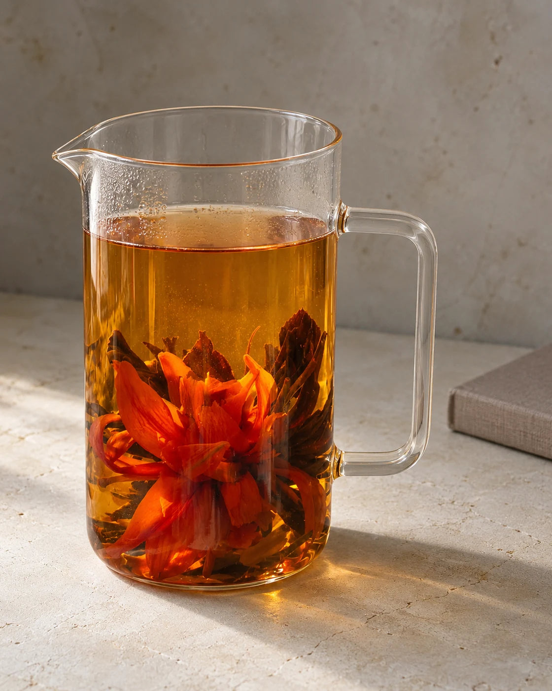 Orange lily blooming black tea in a tall glass pitcher, with open flowers surrounded by unfurled tea leaves.