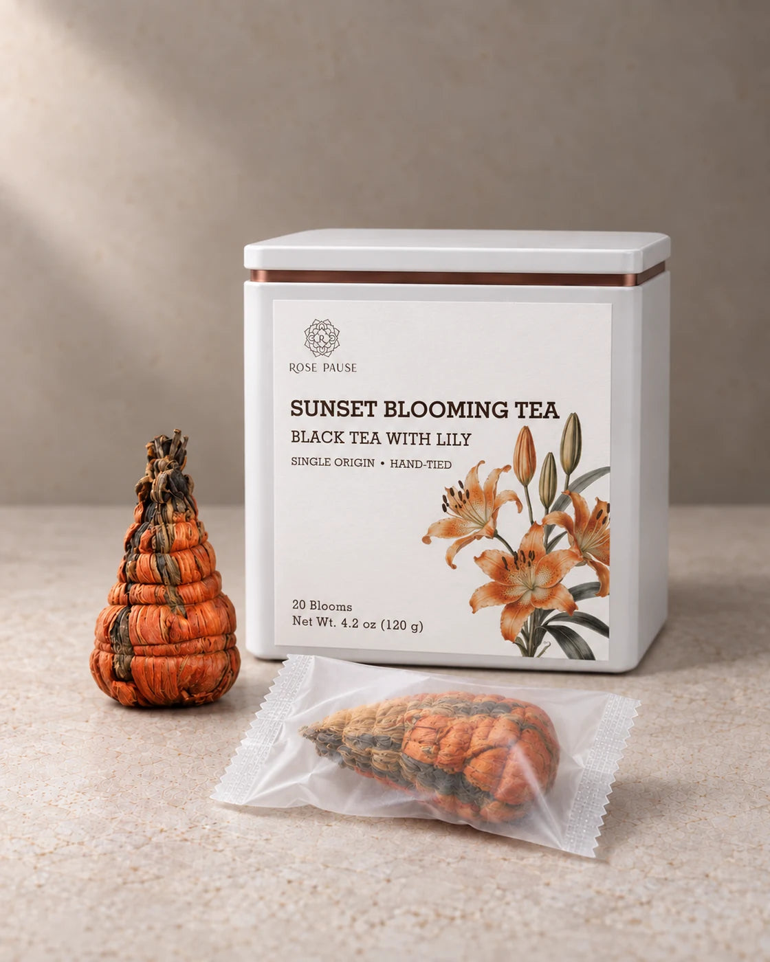 Rose Pause Sunset Blooming Tea tin beside two hand-tied orange lily tea blooms, one individually wrapped.